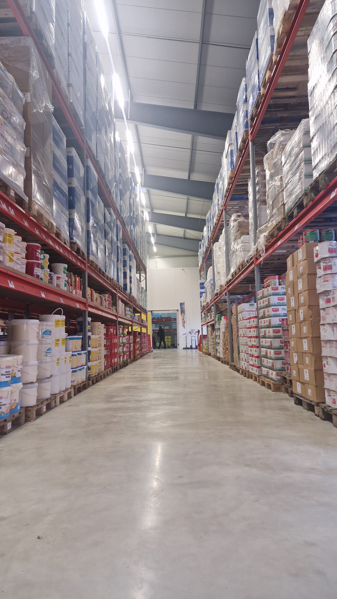 Gänge in einem Lagerhaus mit hohen Regalen, die mit Kartons und Eimern voll verpackter Waren bestückt sind.