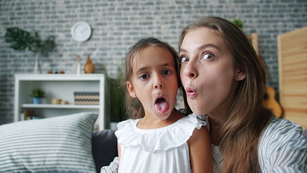POV of funny young woman and cute girl mother and daughter making funny faces taking selfie at home enjoying funny activity. Youth, photos and emotions concept.