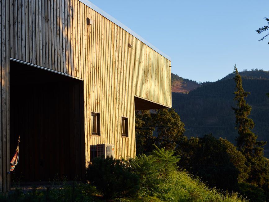 Exterior of rural wooden two storey construction located on grassy slope against green hills on sunny summer day