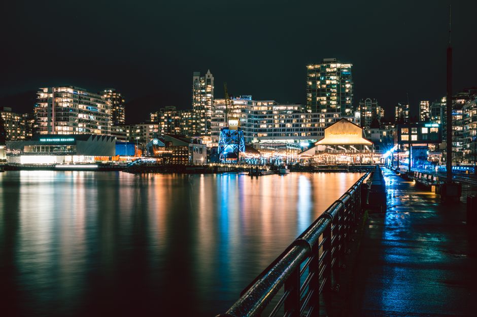 Illuminated waterfront skyline in North Vancouver captured by night, reflecting modern architecture and city lights.