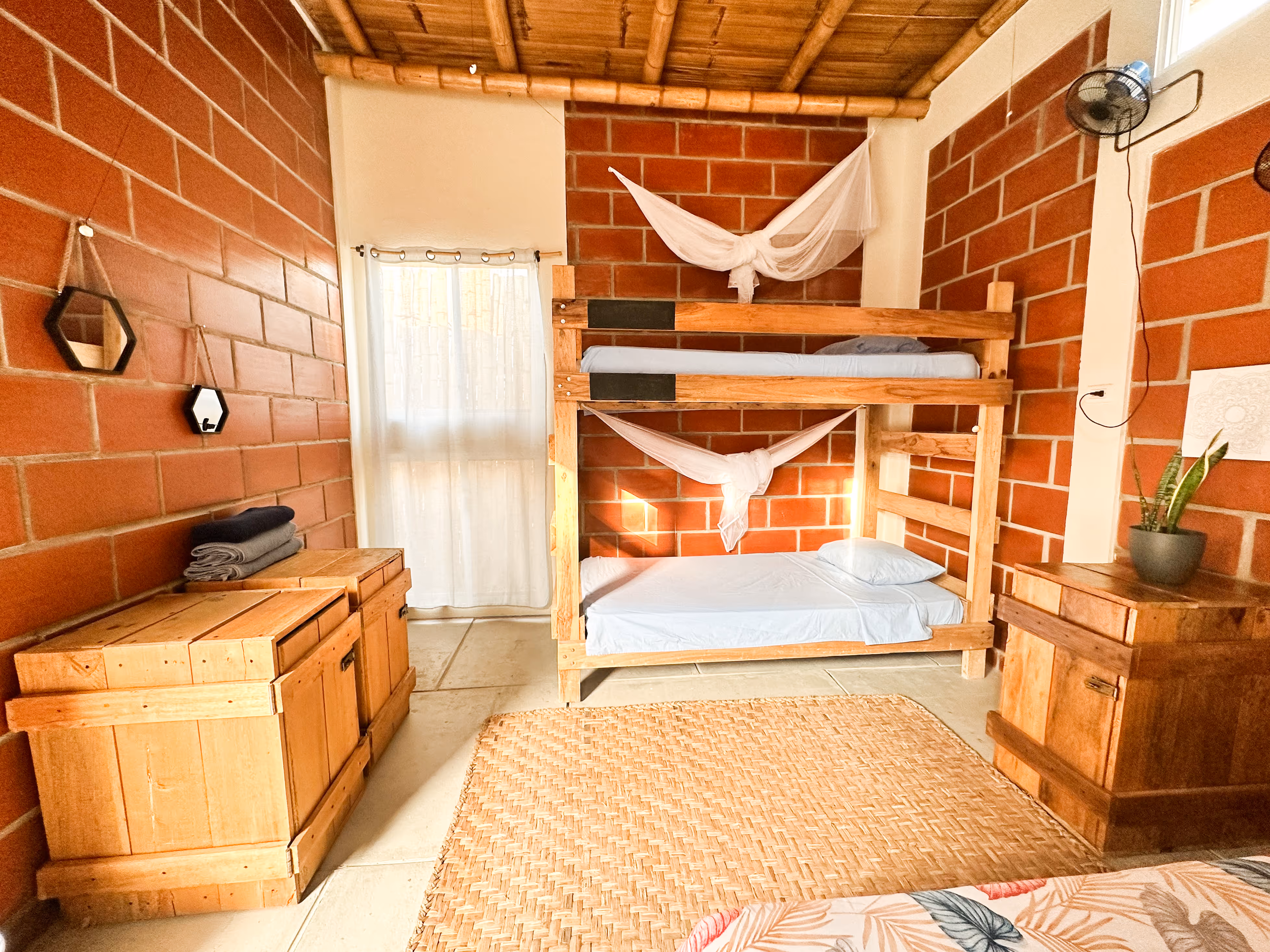 Cozy bedroom with wooden bunk beds, light blue bedding, red brick walls, woven rug, and wooden furniture.
