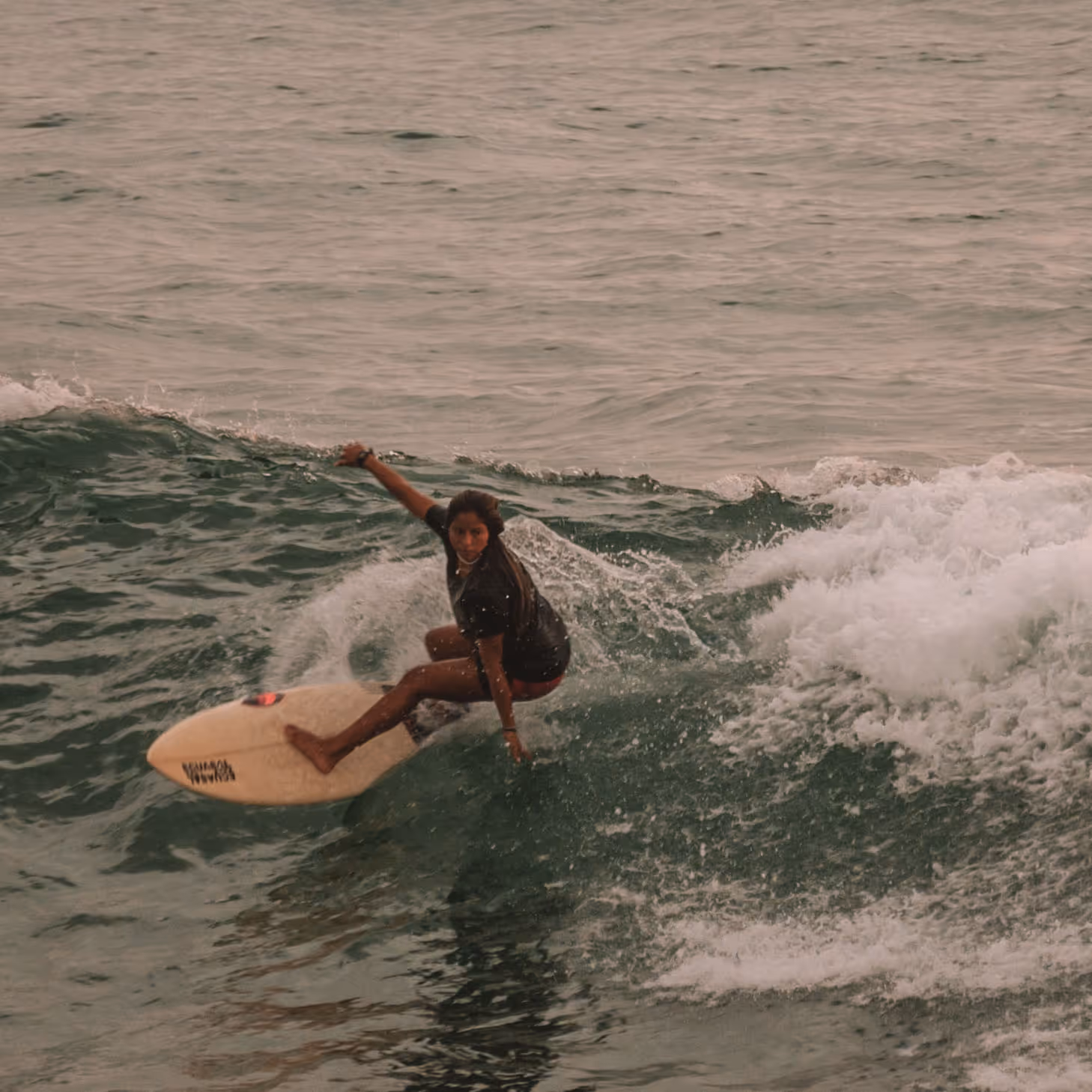 Woman surfing on a wave in the ocean, balancing on a white surfboard.