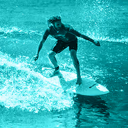 Man surfing on a wave in the ocean wearing a wetsuit top and shorts.