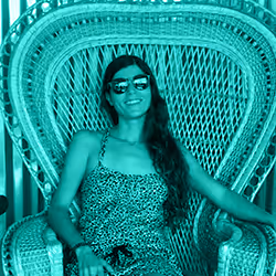 Woman with long hair wearing sunglasses and a patterned dress sitting on an intricately woven chair.