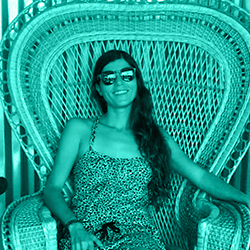 Woman with long hair wearing sunglasses and a patterned dress sitting on an intricately woven chair.