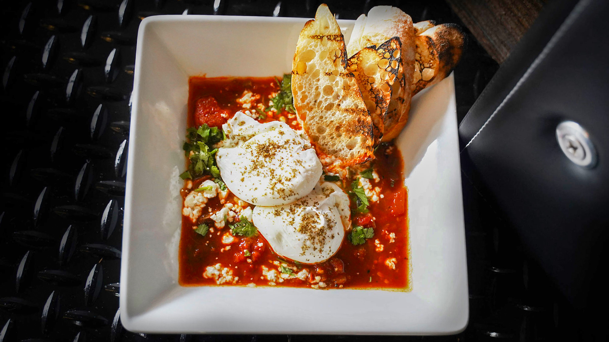 Poached eggs in spiced tomato stew cremini mushroom, pepper topped with goat cheese, cilantro & grilled ciabatta