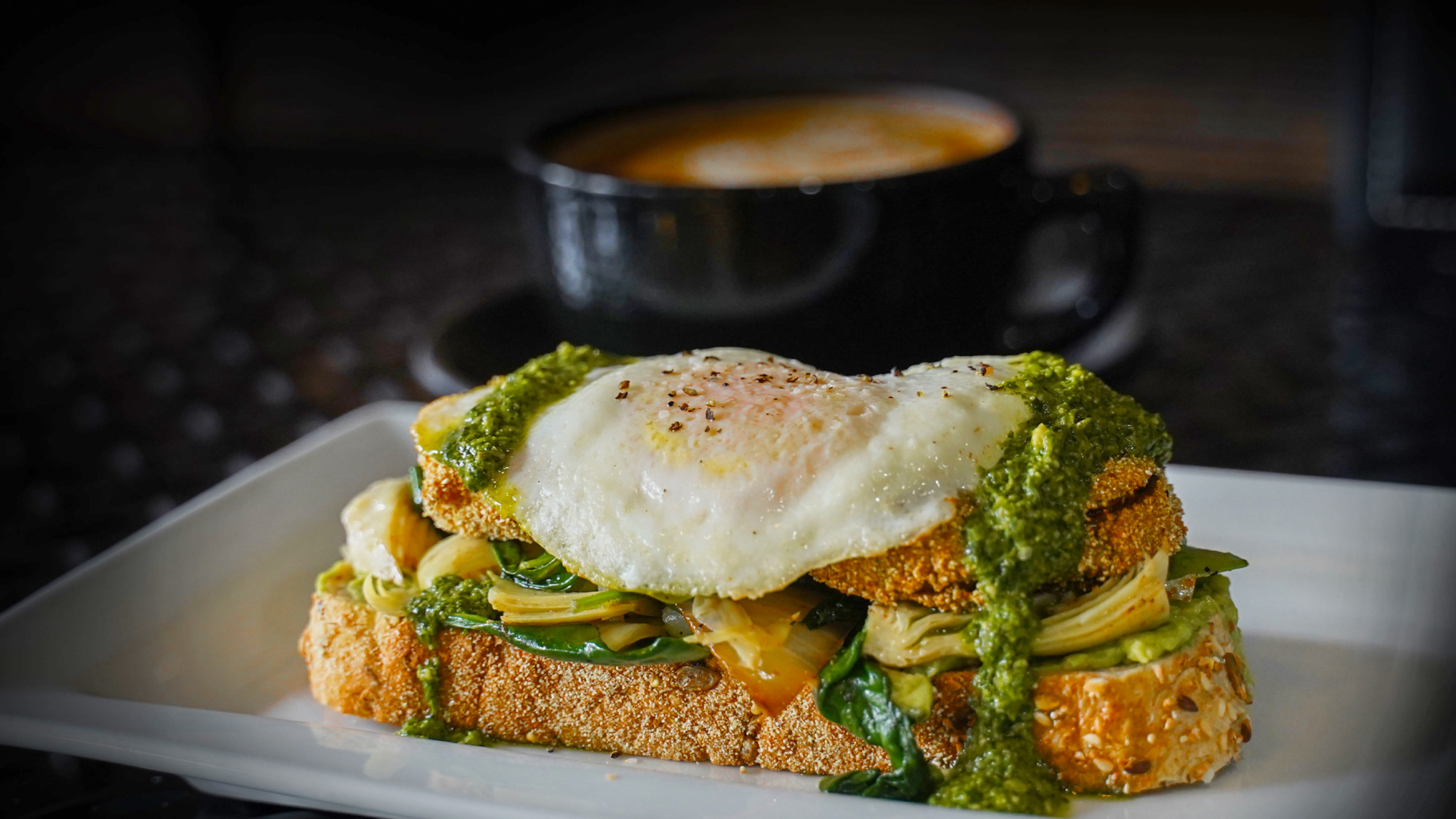 Toasted7 grain topped with smash avocado, fried green tomato sautéed spinach, artichokes hearts, over medium eggs, & pesto.