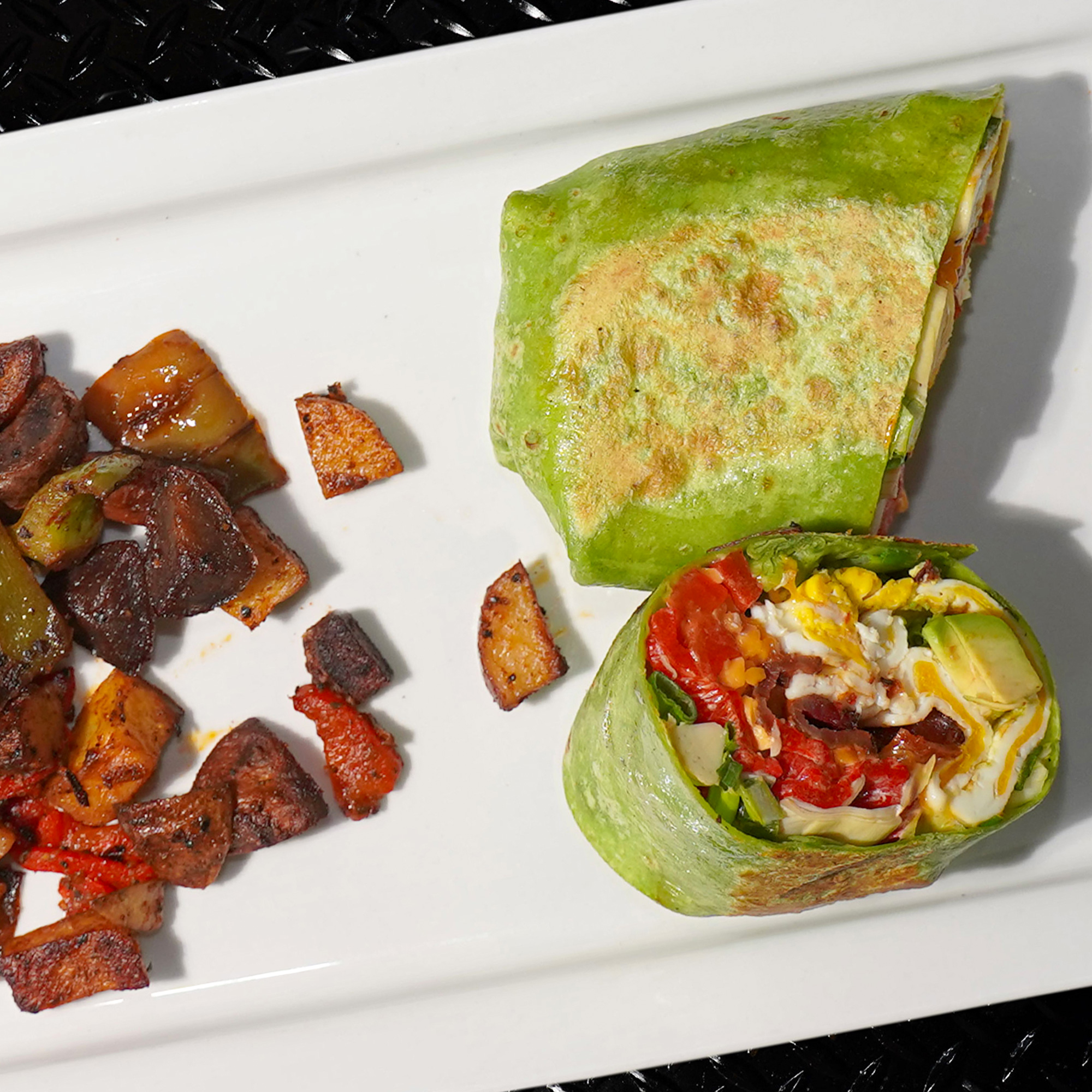 Two eggs over medium, thick cut bacon, artichoke, roasted red peppers, scallions, sharp cheddar cheese, avocado, spicy aioli wrapped in a spinach tortilla, with house potatoes.