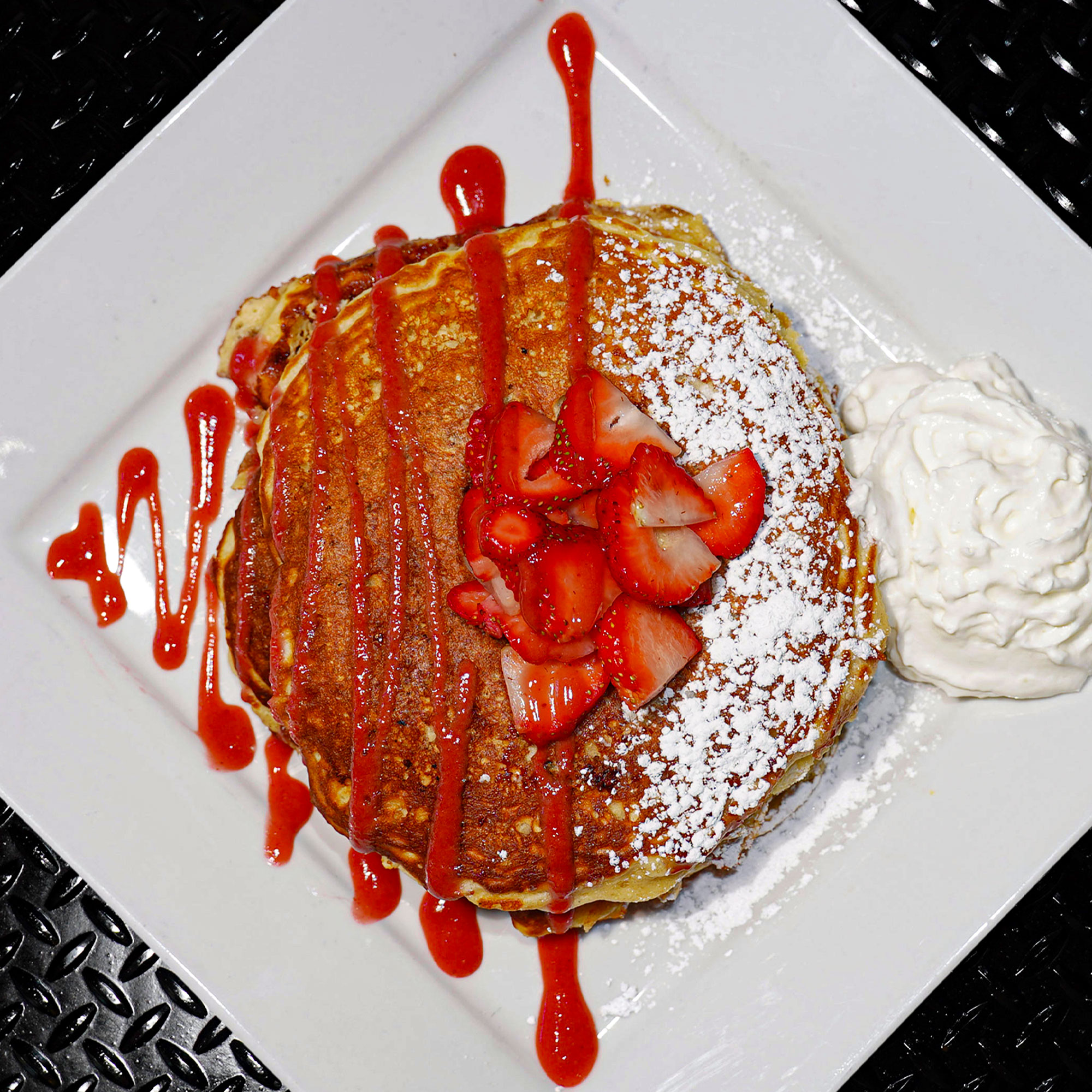 Three strawberry pancakes topped with a house made strawberry  puree, fresh strawberries and powdered sugar.