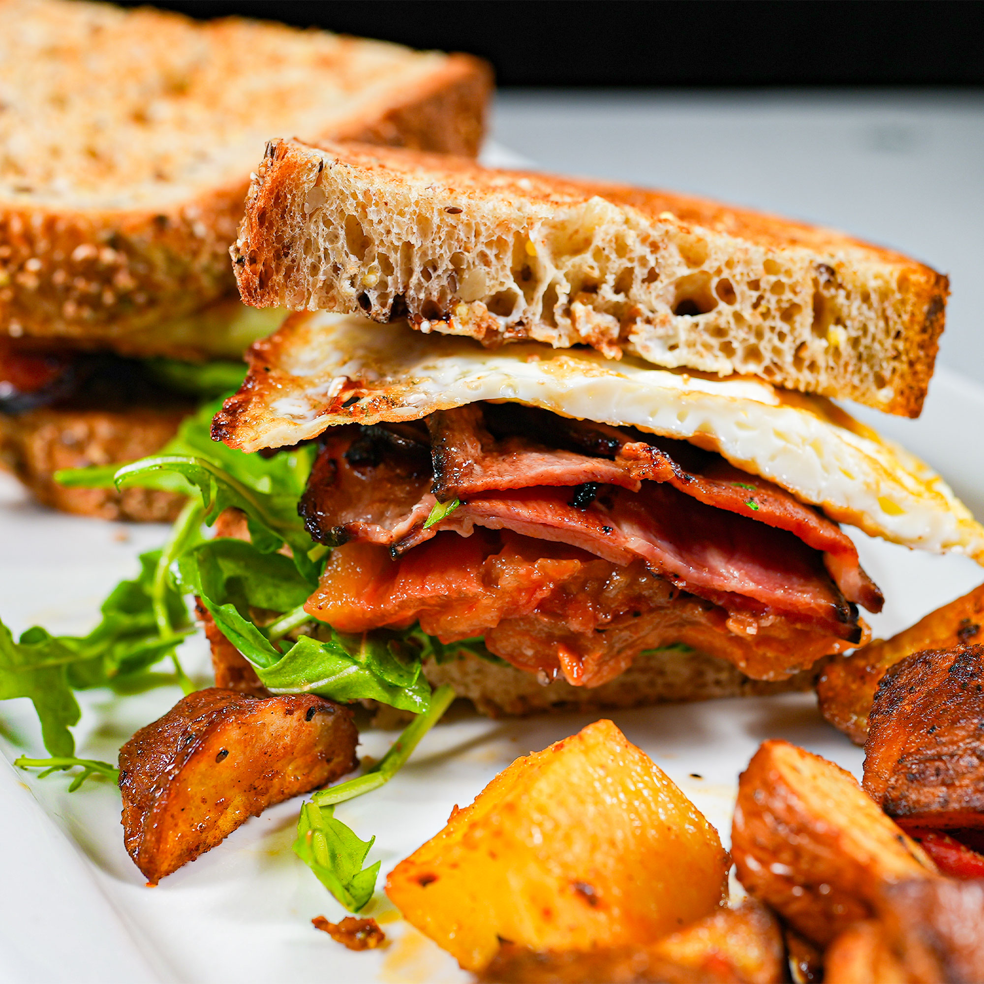 Pork shoulder bacon, fried eggs, tomato confit, arugula, crème fraiche, balsamic reduction on grilled 7 grains with house potatoes.