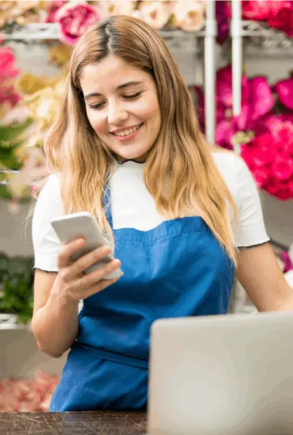 A smiling woman in a gray apron processes a payment at a small business counter in a café