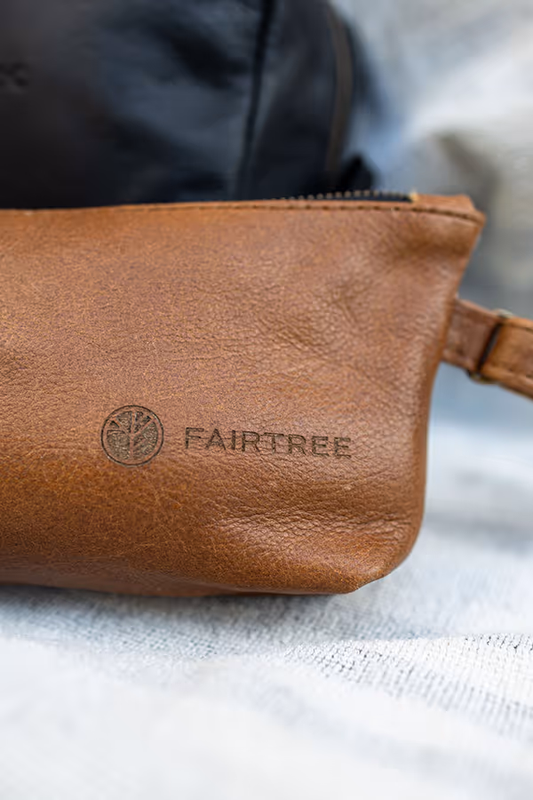 Close-up of a brown leather makeup bag with a zipper and the brand name 'FAIRTREE' embossed next to a tree logo.