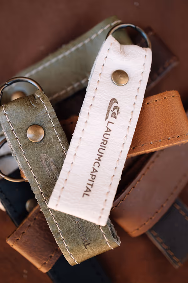 Close-up of leather keyrings in white, green, brown, and black colors with stitched edges and metal rivets.