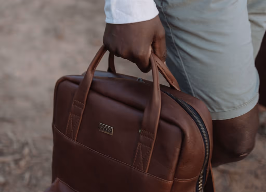 Close-up of a person holding a brown leather briefcase while walking outdoors.