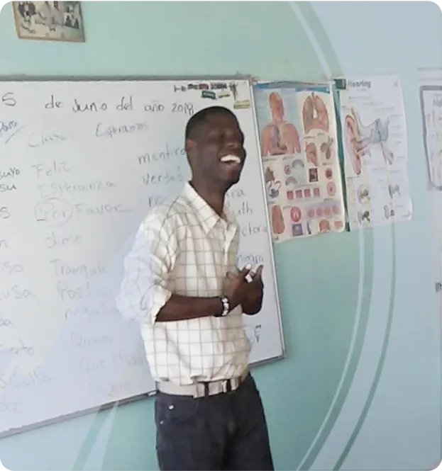 Smiling man standing in front of a whiteboard in a classroom with anatomical charts on the wall.