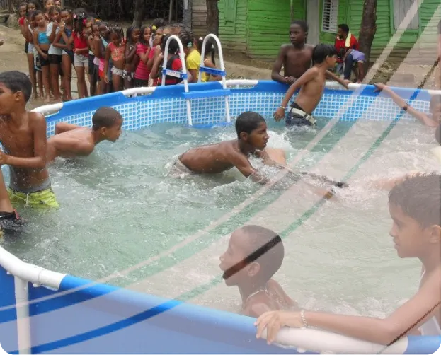 Children swimming and playing in a small above-ground pool with a group of kids waiting outside.