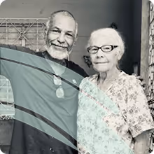 An elderly man, Hector and woman, his mum standing close together, smiling at the camera.