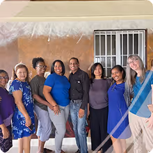 Group of eight diverse women including Vivian, standing in a row inside a room with a window and beige wall.