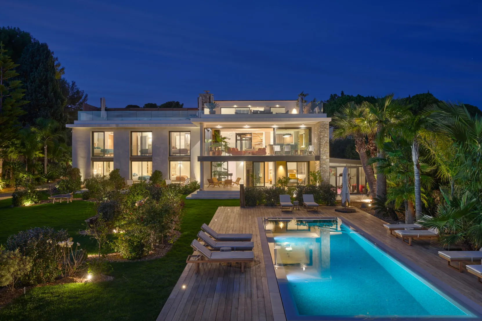 Maison, la villa l'ile verte éclairée la nuit avec piscine bleue entourée de chaises longues et jardin paysager, La Ciotat.