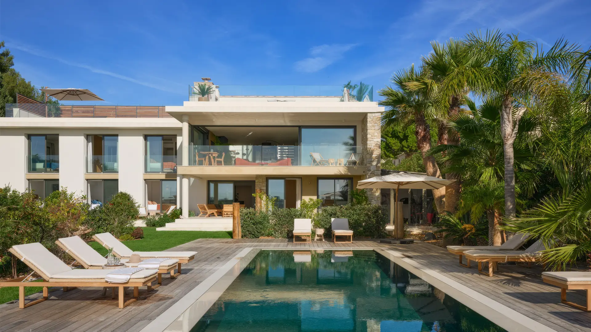 Vue arrière de la villa l'île verte avec terrasse, piscine bordée de chaises longues et des palmiers.