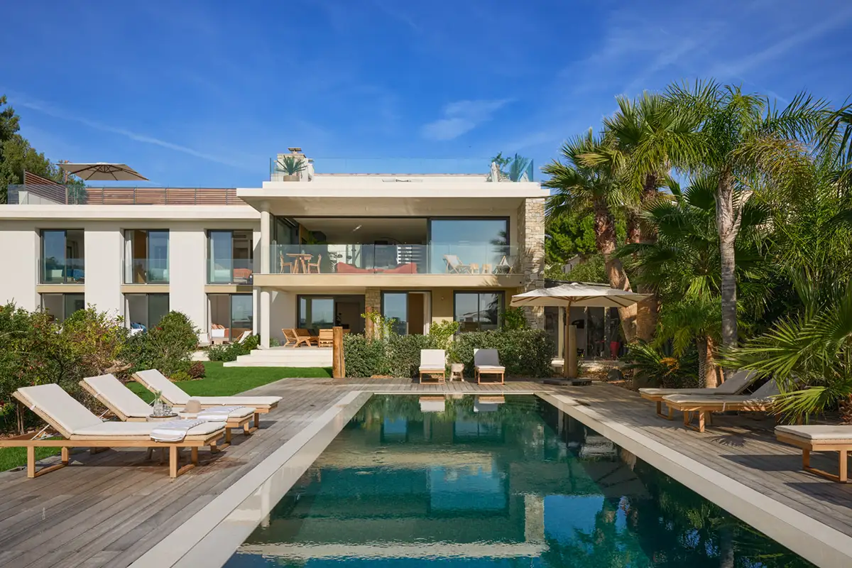 Piscine miroir entourée de terrasses en bois et façade contemporaine de La Villa L’Île Verte dans un jardin méditerranéen