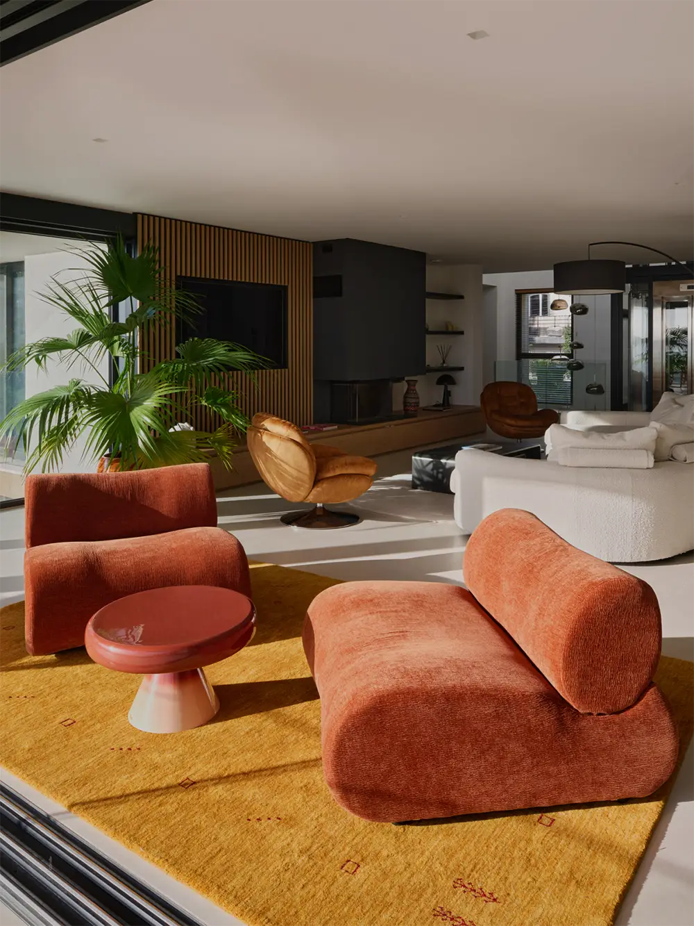 Salon spacieux de la villa l'île verte, avec fauteuils et canapé orange sur un tapis jaune, plantes vertes, et cheminée moderne. La Ciotat