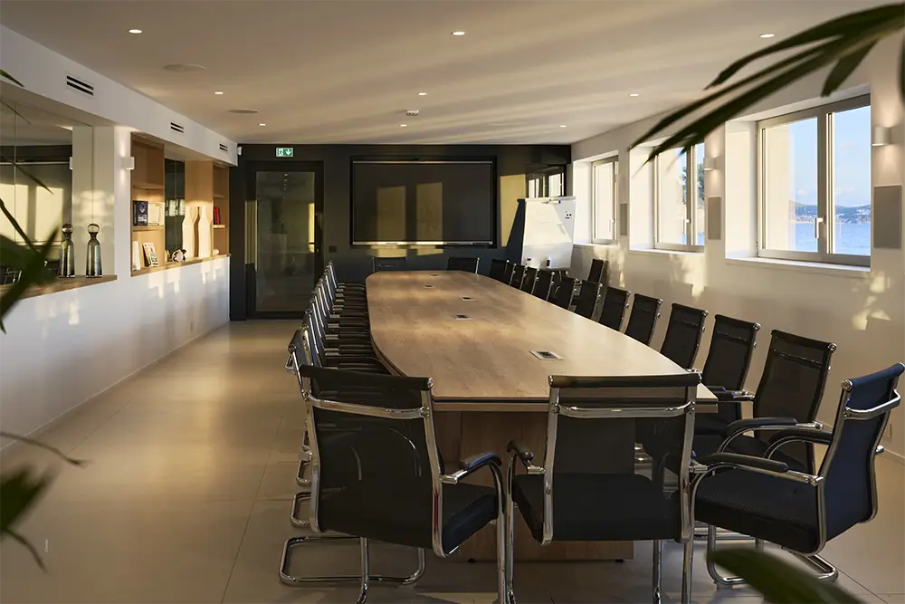business center moderne avec grande table de réunion en bois et chaises noires, baigné de lumière naturelle avec vue mer dans le pavillon de la villa de luxe L’Île Verte à La Ciotat