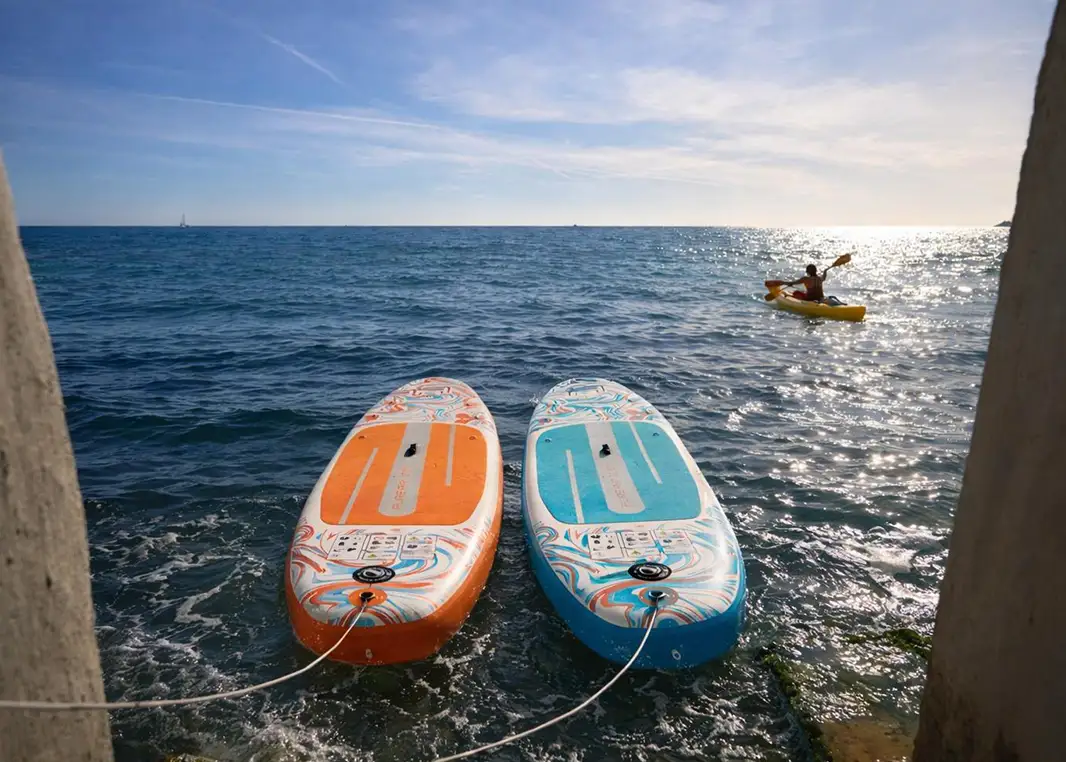 Planches de paddle orange et bleu sur la mer, kayakiste au loin sous un ciel ensoleillé, Villa L’Île Verte, La Ciotat.