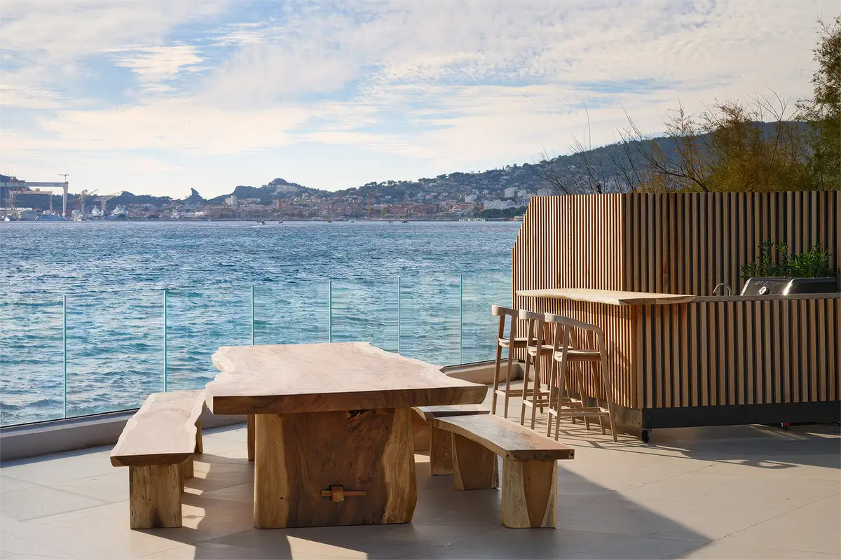 La Villa l'île verte, illuminée de nuit avec une piscine mirroir et des chaises longues sur une terrasse en bois entourée de végétation. La Ciotat