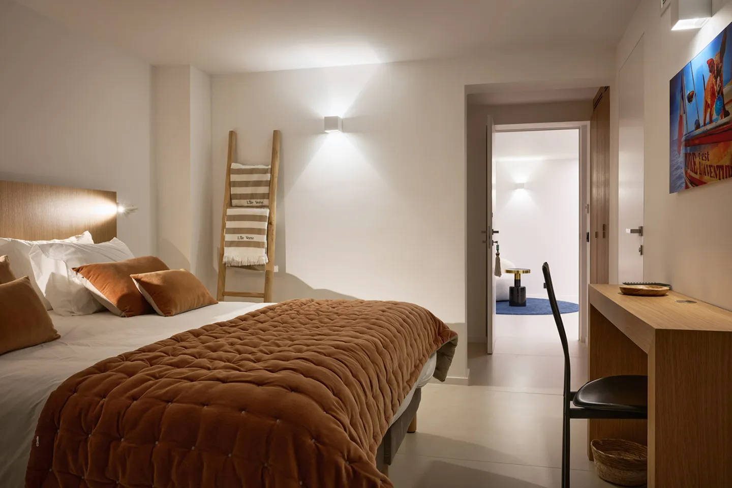 Chambre 8 moderne avec grand lit double, couverture et coussins couleur terre cuite, vue sur la mer par une baie vitrée