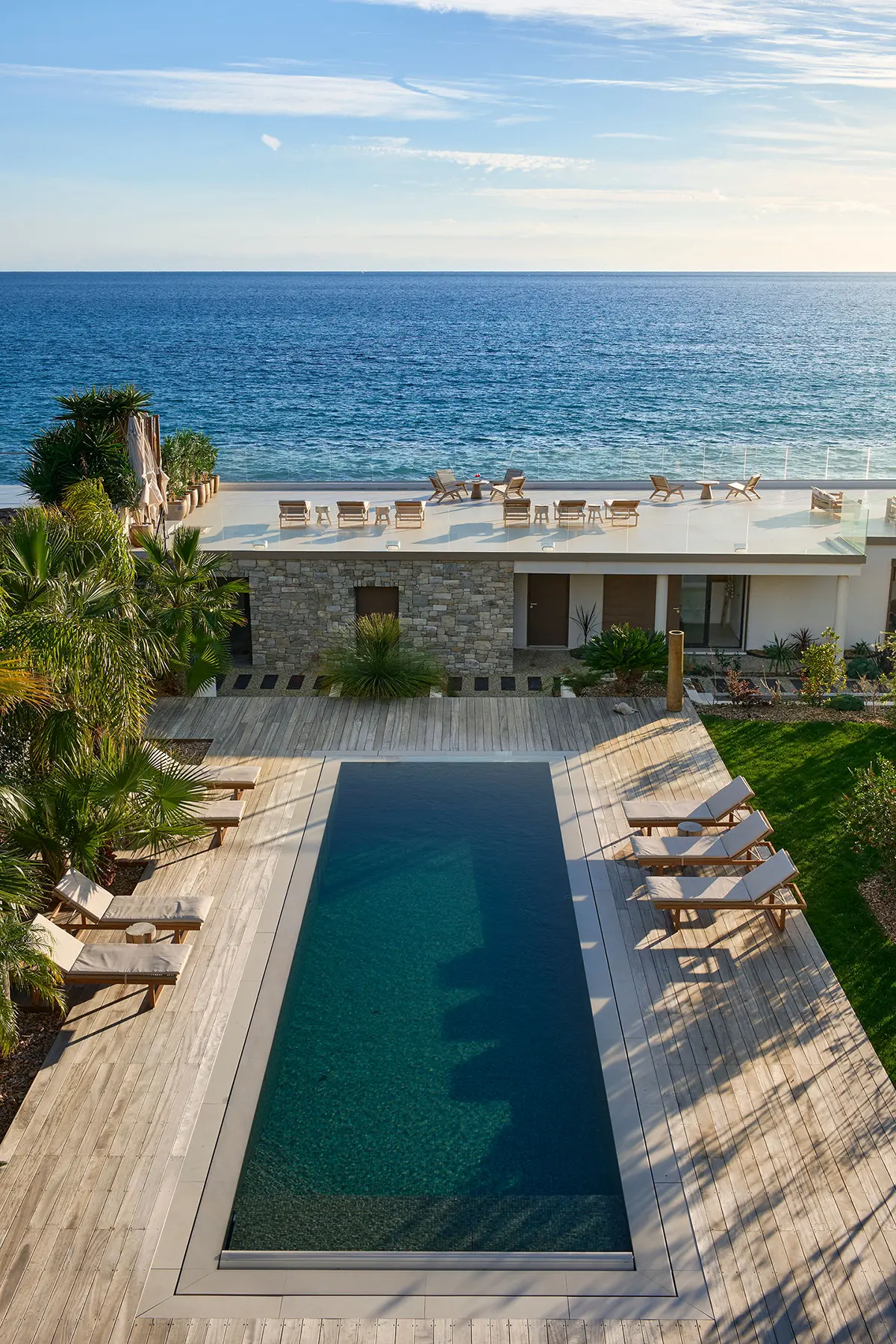 Piscine miroir chauffée de la Villa L'Île Verte entourée de chaises longues, palmiers et pelouse avec vue sur la mer, La Ciotat