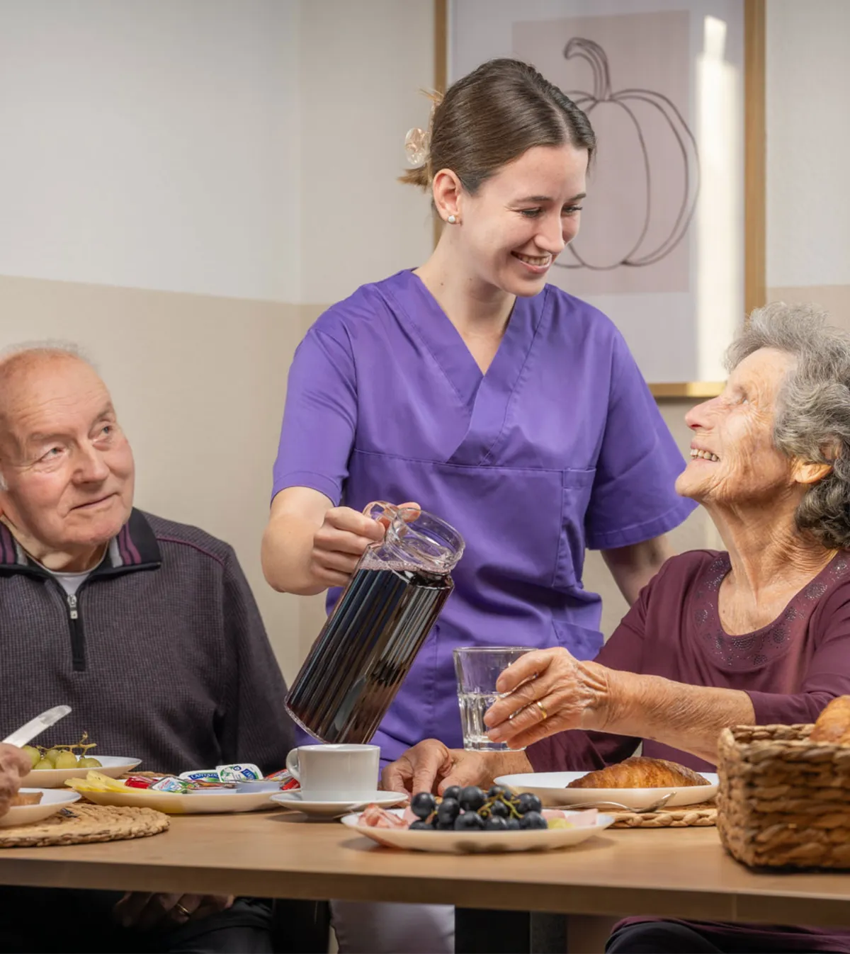 Eine Fachangestellte Gesundheit schenkt einer älteren Frau Tee ein beim Frühstück
