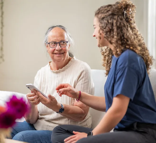 Junge Frau erklärt einer älteren Frau am Smartphone etwas