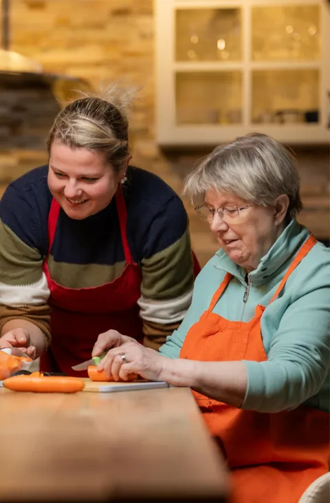 Jüngere Frau hilft einer älteren beim Kochen mit Gemüse