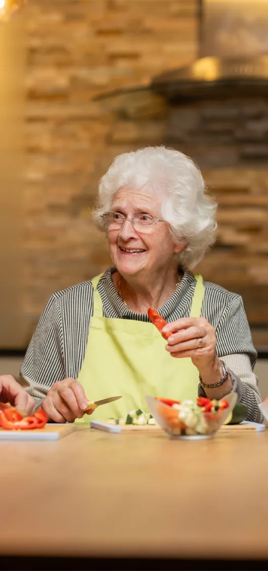 Eine Frau sitzt am Tisch und schneidet Gemüse und hat Spass dabei