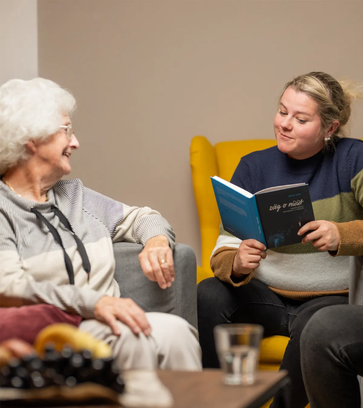 Frau liest aus einem Buch einer älteren Dame vor