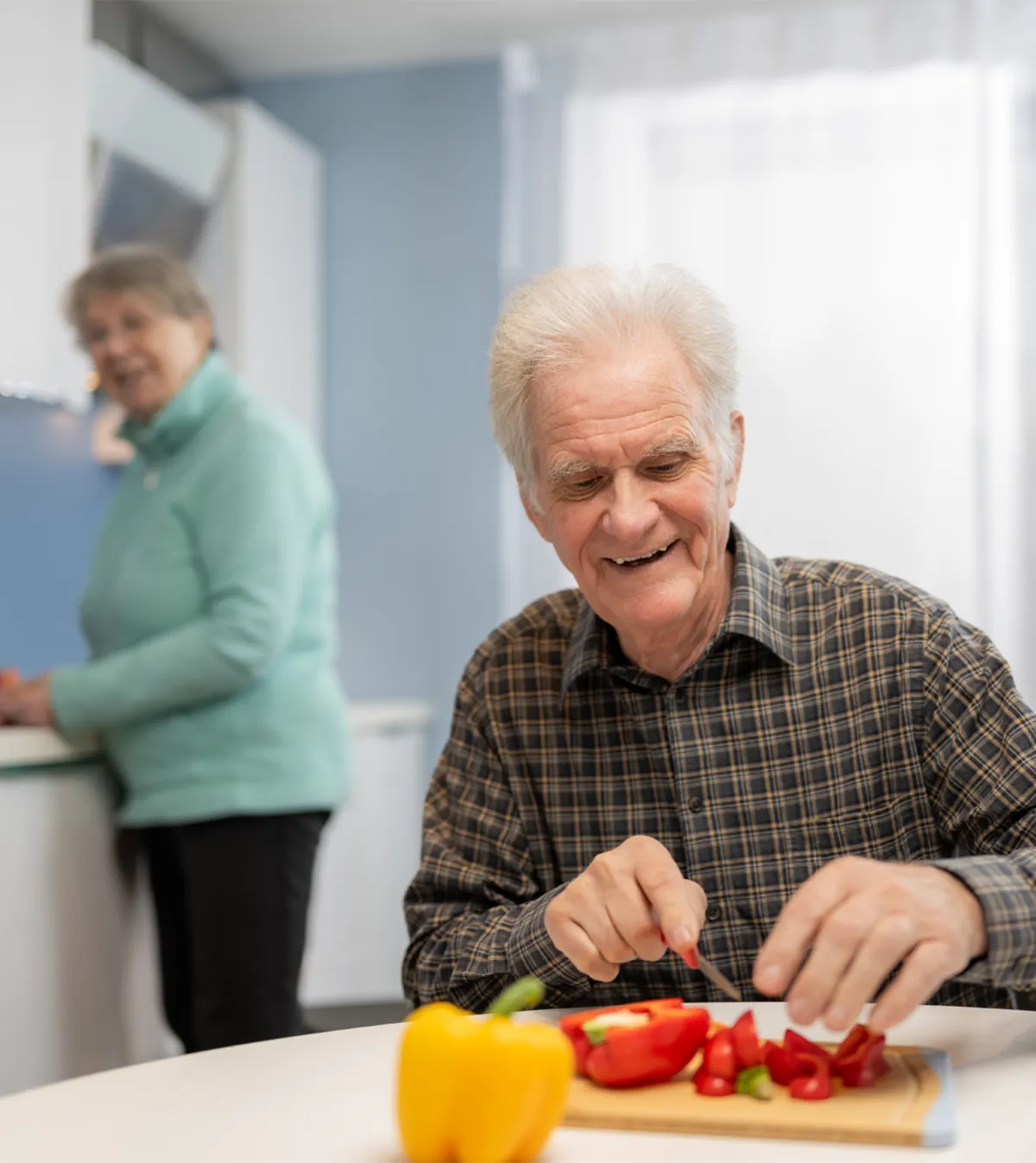 Mann schneidet Gemüse in der Küche, seine Frau wischt das Gemüse
