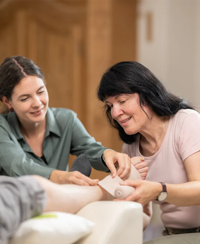 Eine Frau zeigt einer anderen, wie sie den Kompressionsverband anlegen muss