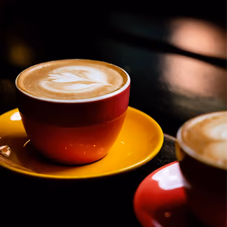 Cappuccino mit Latte Art in roter Tasse auf gelber Untertasse