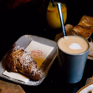 Croissant mit Staubzucker, Milchkaffee und Orangensaft zum Frühstück