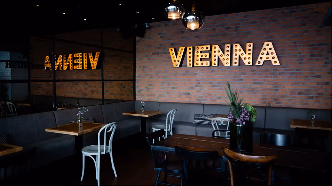 Innenraum von Tesla Coffee & Concept in Wien mit beleuchtetem VIENNA Schriftzug an der Ziegelwand