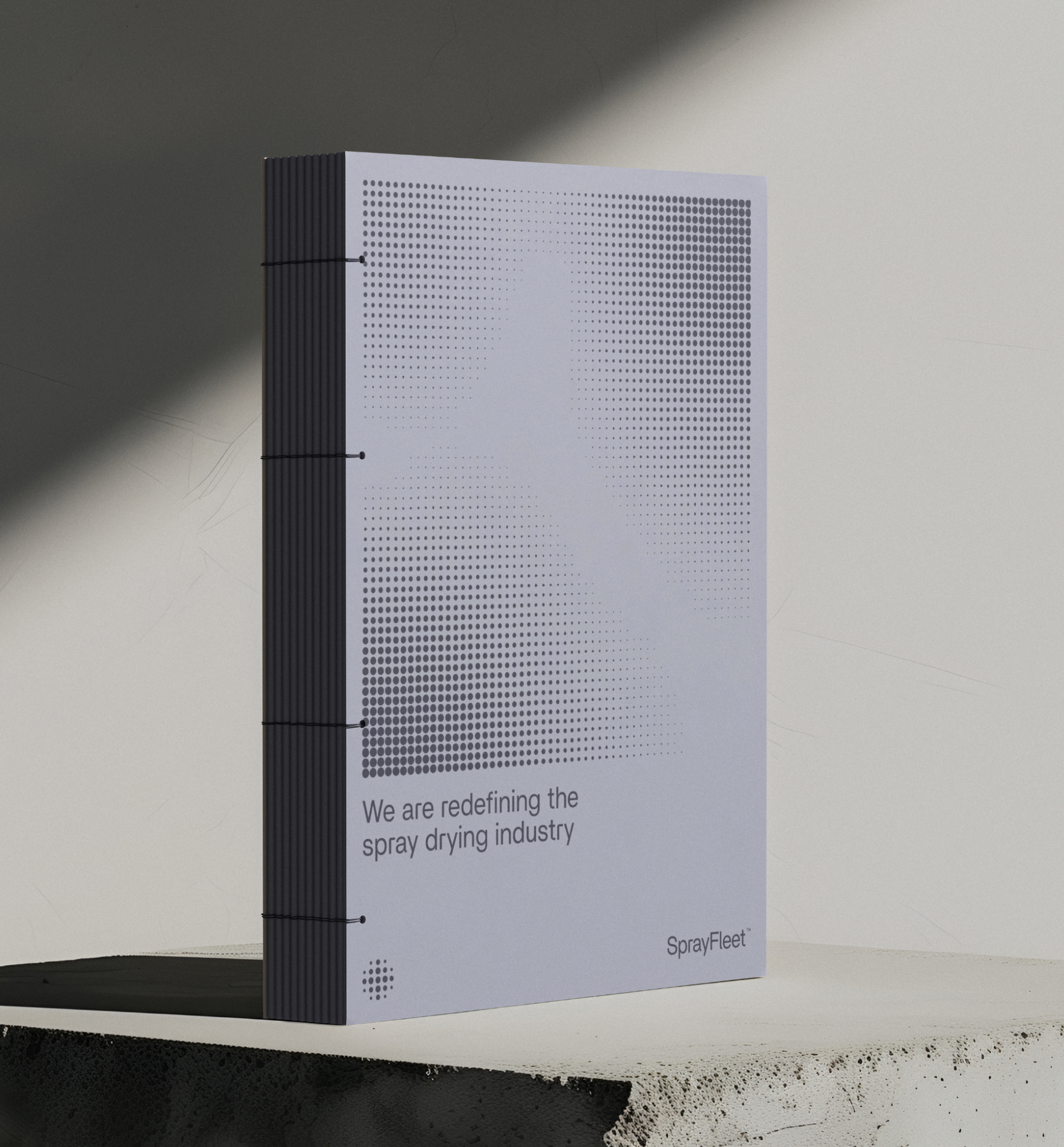 Ringbind med prikket design og teksten "We are redefining the spray drying industry" samt SprayFleet-logo på struktureret overflade.