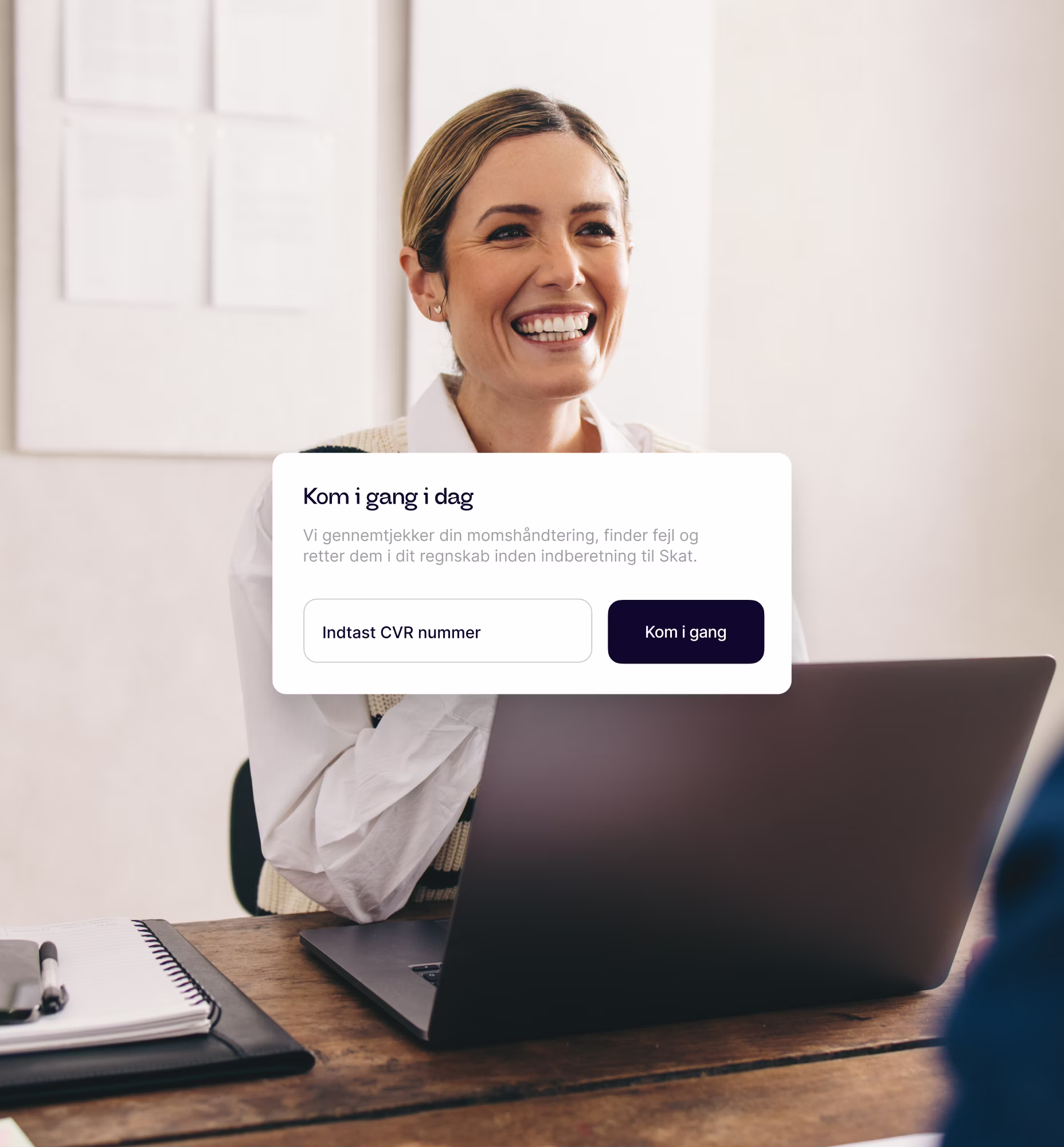 Smilende kvinde ved træbord med laptop og notesbog samt dansk tekstoverlay om at starte momshåndtering i dag.
