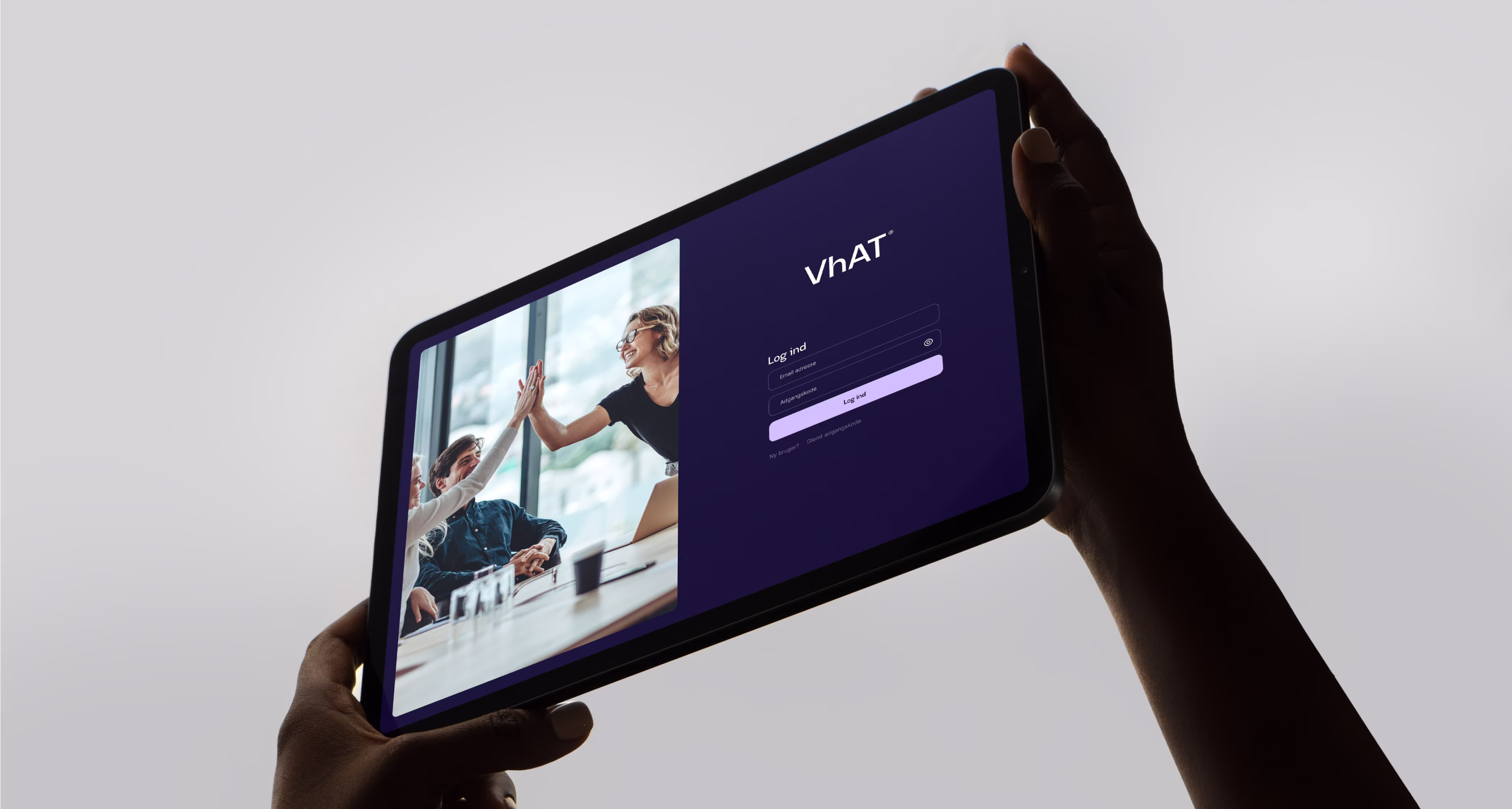 Person der holder tablet med login-skærm med VhAT-logo og team der giver high-five i baggrunden.