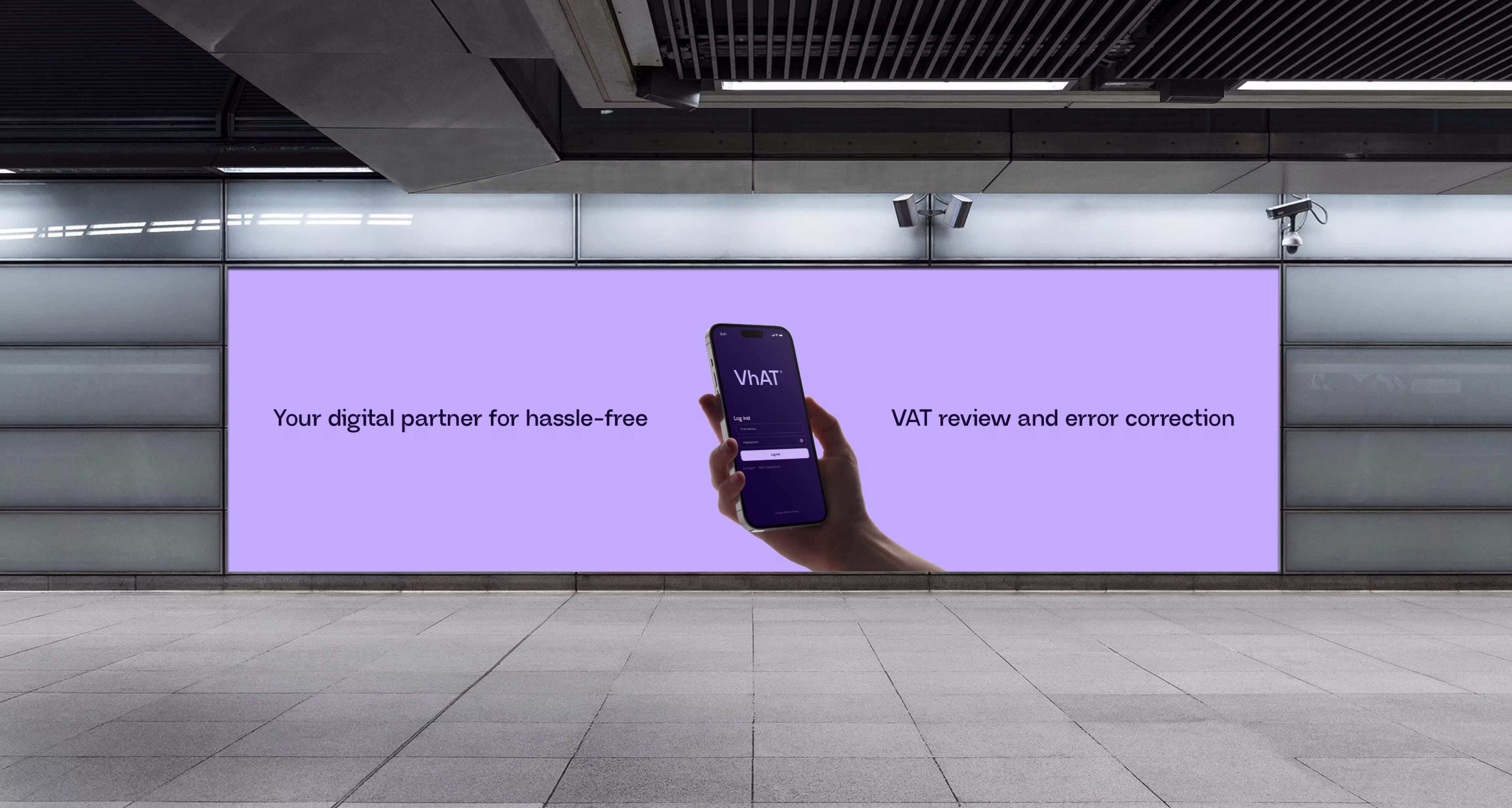 Billboard i metro med hånd der holder telefon med login-skærm til VhAT-app og tekst om din digitale partner til nem moms-gennemgang og fejlkorrigering.