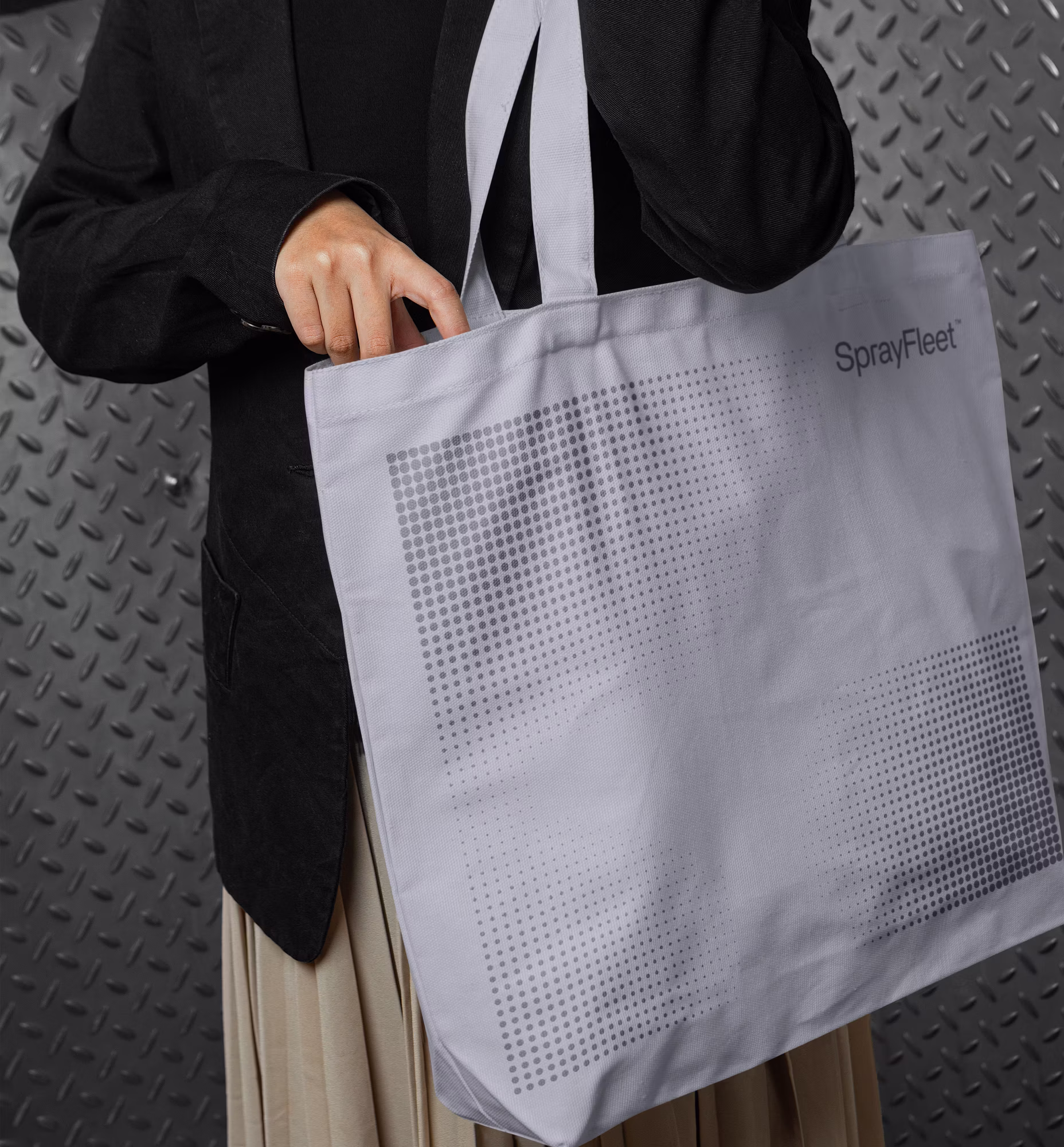 Person der holder hvid SprayFleet-mulepose med prikket firkant-design foran riflet metalbaggrund.