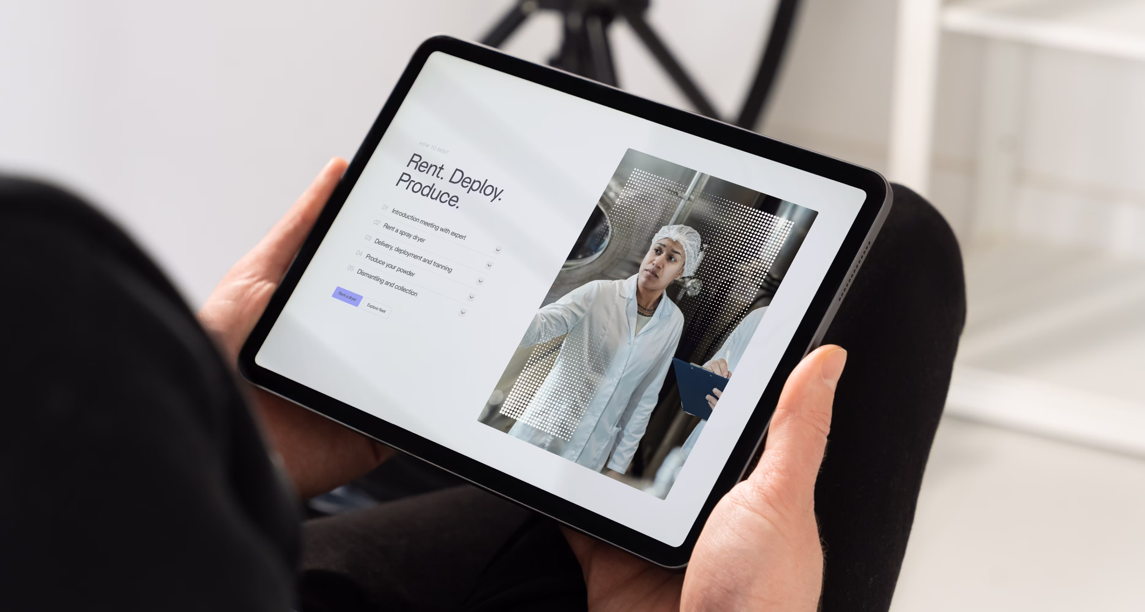 Person der holder tablet med webside med titlen "Rent. Deploy. Produce." med tjekliste og foto af laboratorietekniker i hvid kittel og hårnet.