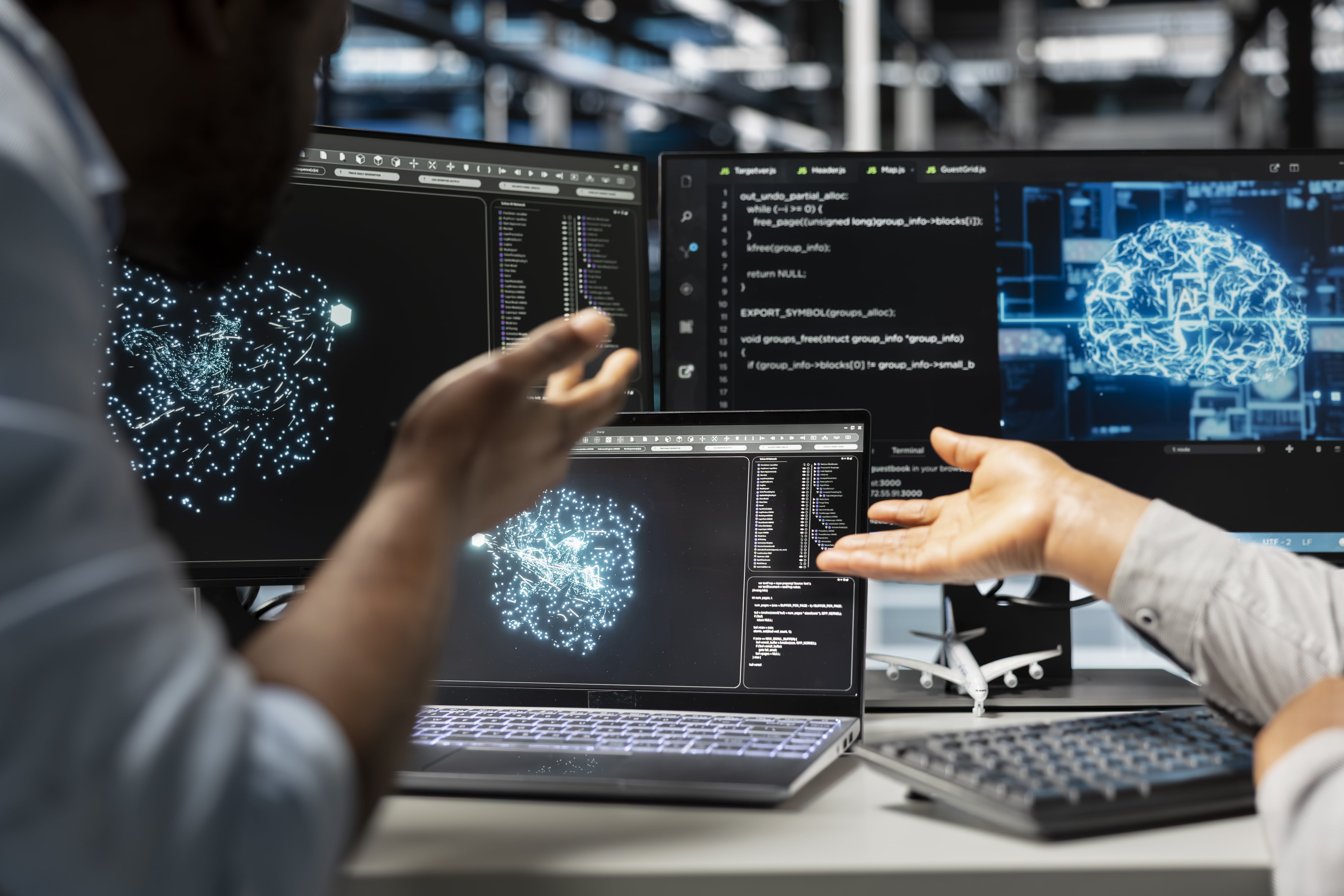 Two engineers discussing data visualizations and code on multiple computer screens in a modern office.