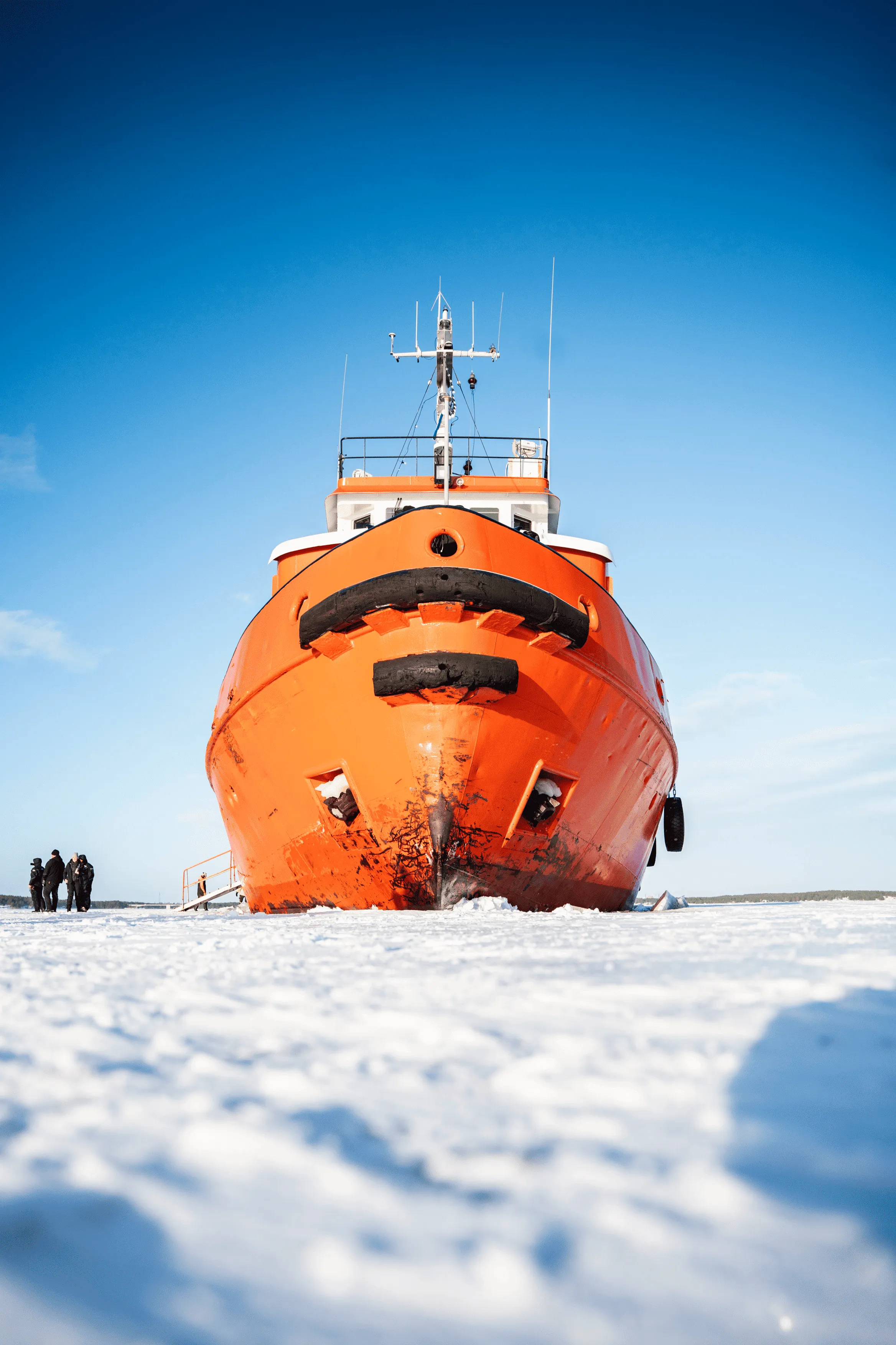 Front view of a large orange icebreaker ship frozen in snow with a clear blue sky.