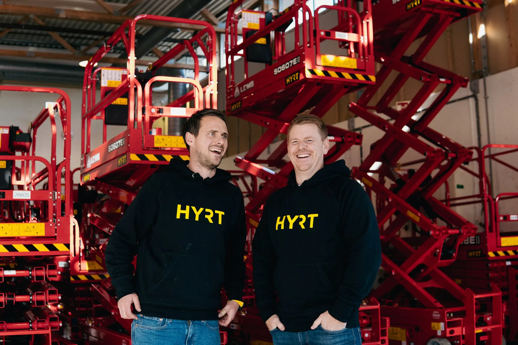 Kenneth Fløysvik og Petter Midbøe Lunde ler sammen foran sakseliftene i hallen